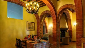 A dining area with a table set for four, surrounded by brick arches, a chandelier, and a fireplace. - Cozy Villa for Six Guests (Sinalunga)