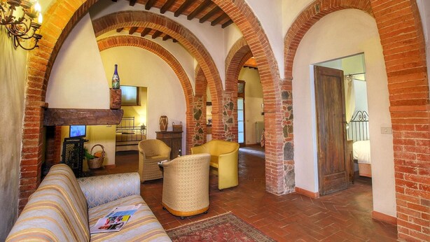 A spacious living room with a sofa, armchairs, and a coffee table. The room features exposed brick arches and a fireplace. - Cozy Villa for Six Guests (Sinalunga)