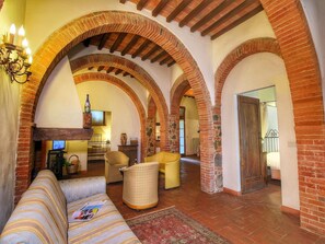 A spacious living room with a sofa, armchairs, and a coffee table. The room features exposed brick arches and a fireplace. - Cozy Villa for Six Guests (Sinalunga)