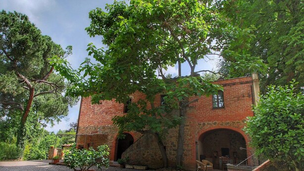 Um edifício histórico com fachada de tijolos, arcos de pedra e um pátio de cascalho.
