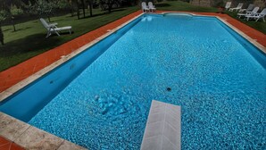 Piscina retangular com água azul cristalina, rodeada por um deck ladrilhado vermelho e espreguiçadeiras brancas.