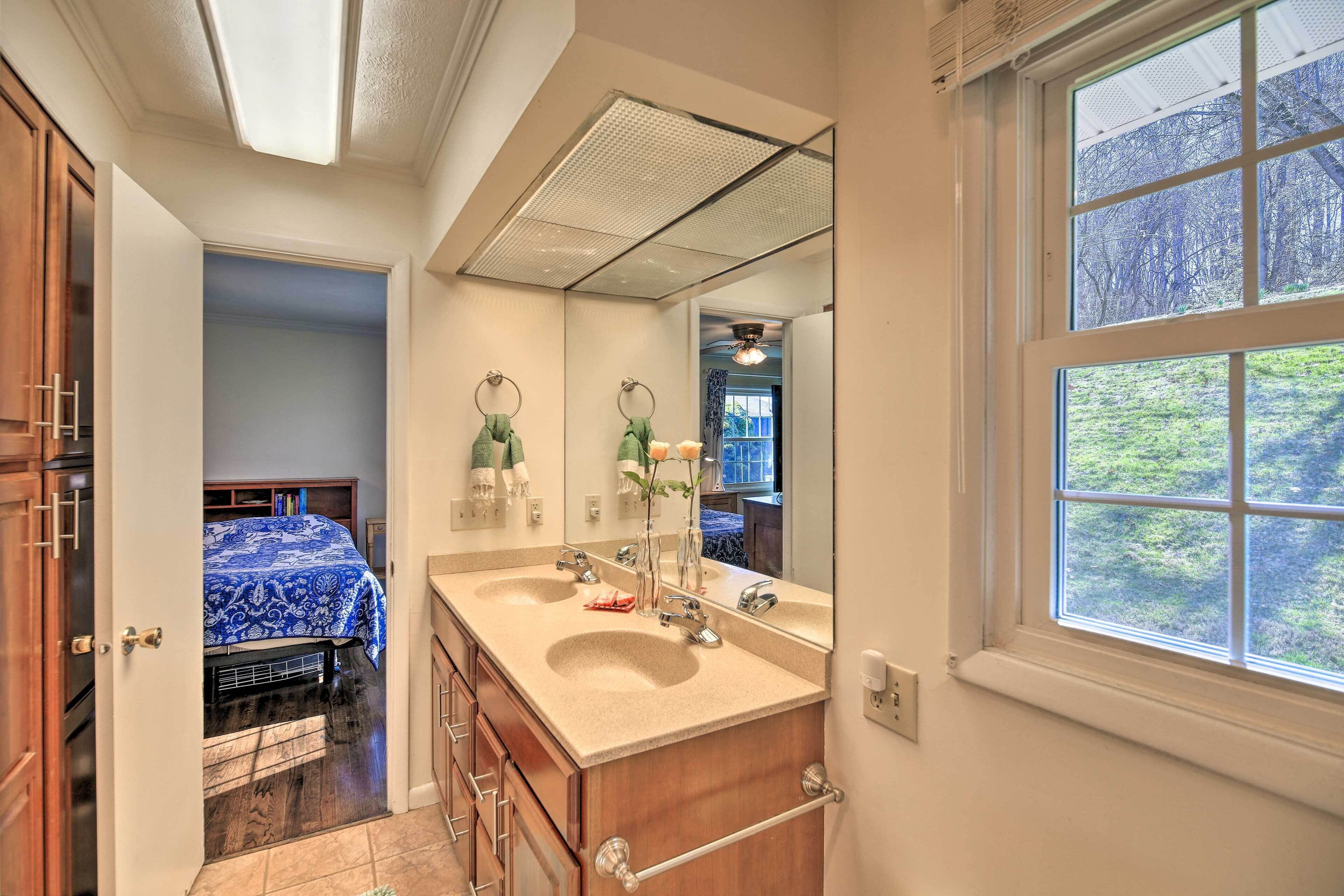 A bathroom with a large mirror, double sink, and a window with a view of trees.