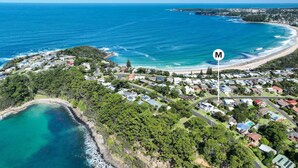 An aerial view of a coastal residential area with houses, a beach, and a clear view of the ocean. - Rockpools in Mollymook (Mollymook Beach)