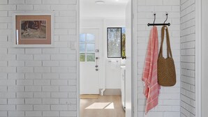 A hallway with white brick walls, a framed picture, a door with a window, and a towel rack with a bag and a towel. - Rockpools in Mollymook (Mollymook Beach)