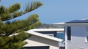 A modern house with a sloped roof, a visible window, and a view of a coastal area with buildings in the distance. - Rockpools in Mollymook (Mollymook Beach)