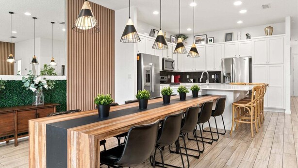 Una cucina moderna con isola in legno, sedie nere e lampade a sospensione.