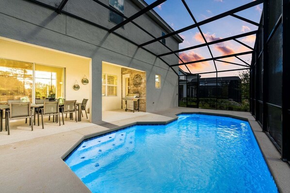 Una piscina interior con techo de vidrio, un comedor con sillas y mesas, y una cocina con mostrador y armarios.