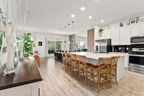 A modern kitchen with a central island, bar stools, stainless steel appliances, and a view to the outdoors.