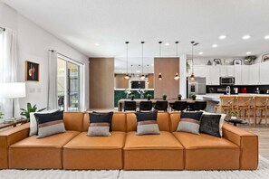 A modern living room with a sectional sofa, a dining area, and a kitchen.