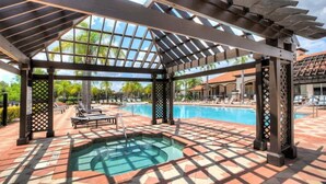 Un'area piscina esterna coperta con idromassaggio, lettini prendisole e una pergola.