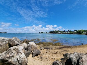 Une plage avec de gros rochers au premier plan, un ciel bleu dégagé et une mer calme.