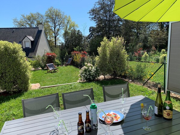 Une terrasse avec une table dressée pour le repas, des chaises d’extérieur et un parasol jaune.