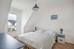 Une chambre à coucher avec un lit, des tables de chevet, un bureau, une fenêtre et un luminaire au plafond.