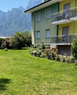 Un immeuble doté d’une façade verdoyante, d’un balcon orné de rampes en métal et d’un jardin bien entretenu, agrémenté de fleurs et de pelouse.