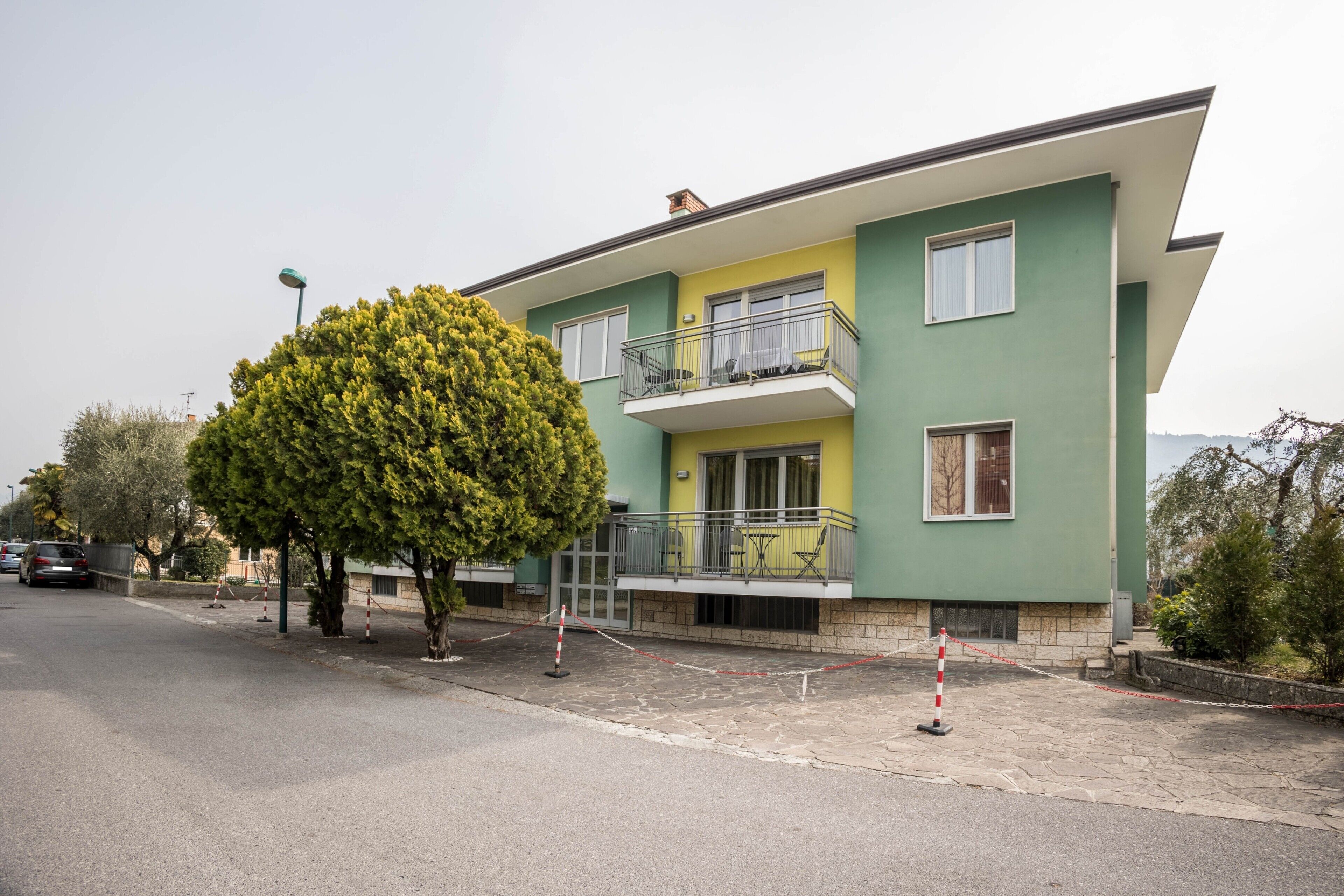 Un bâtiment à deux étages doté d’un balcon, avec un arbre devant et une zone pavée.