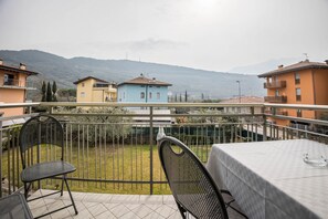 Un balcon avec des chaises et une table, donnant sur un quartier résidentiel avec des maisons et des montagnes.