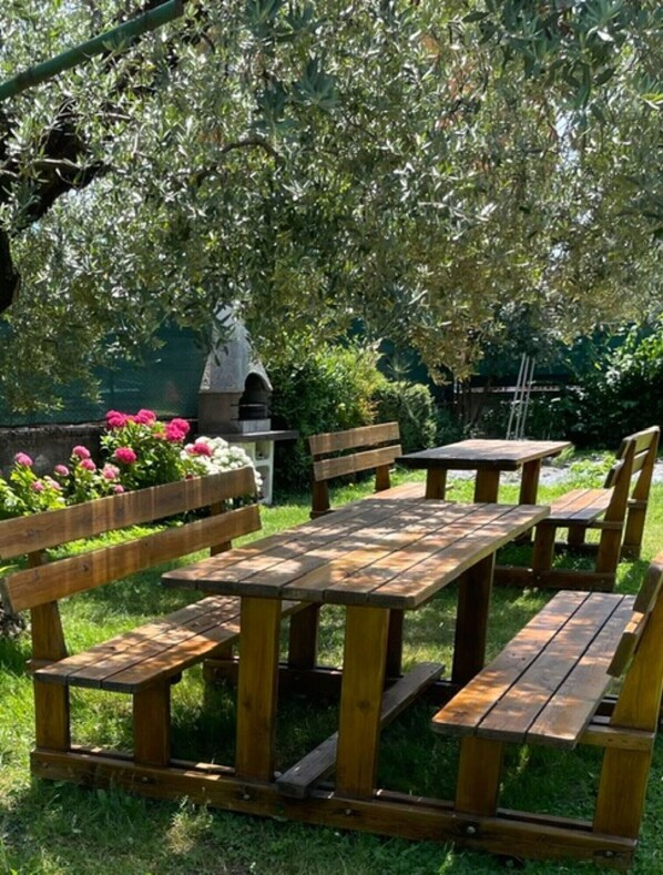 A wooden picnic table and benches in a garden with a stone structure and flowering plants.