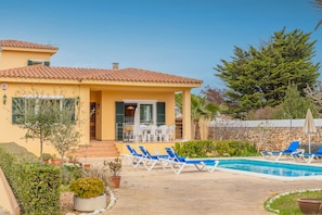Un bâtiment jaune avec un toit en tuiles, une piscine et des chaises longues bleues.