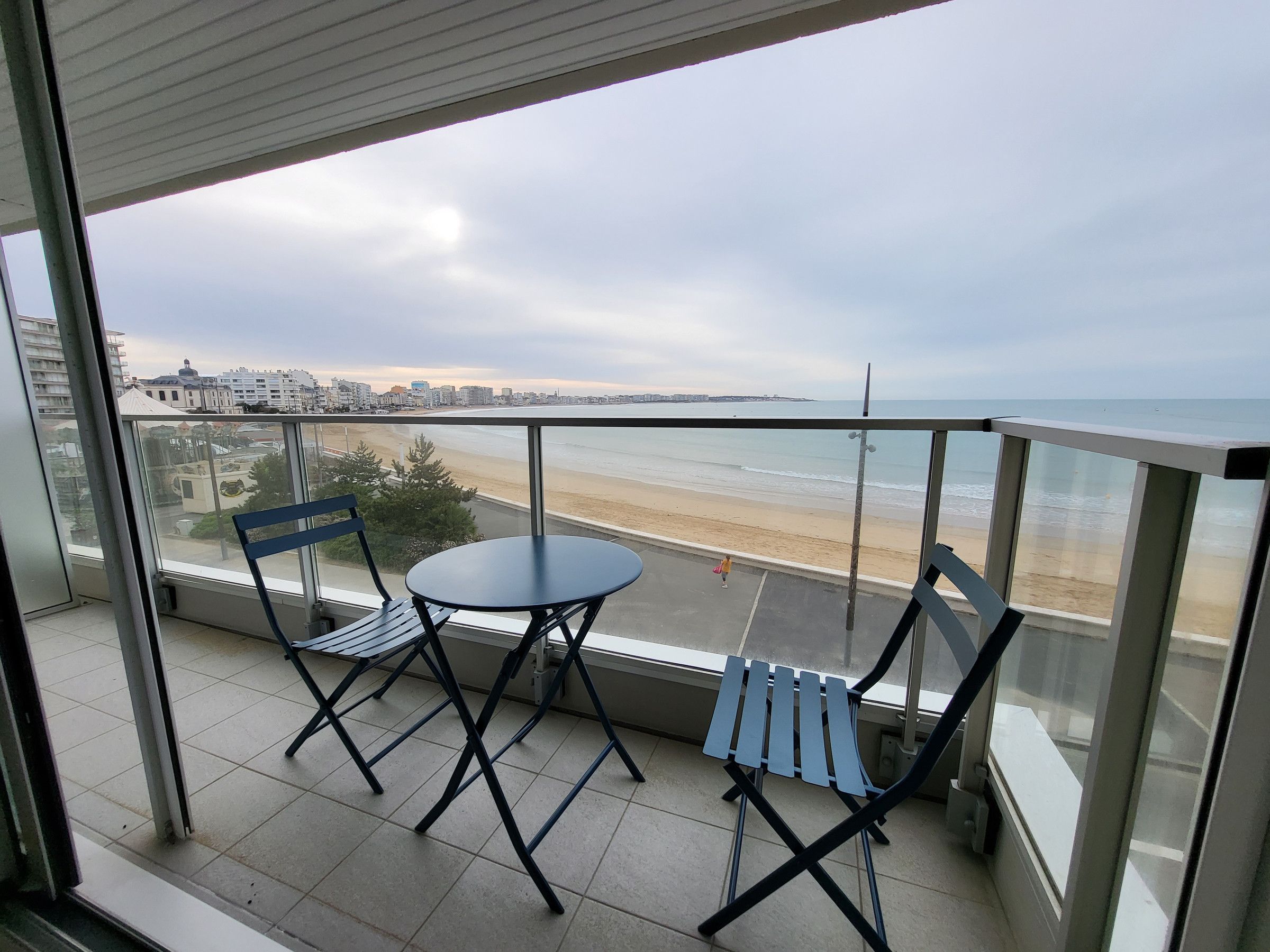 A balcony with two chairs and a table, overlooking a beach and cityscape.