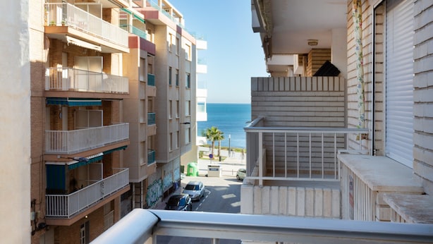 A multi-story building with balconies, a view of the sea, and a street with parked cars. - Apartment "Nav 4C 4pC" with Sea View & Terrace (Torrevieja)