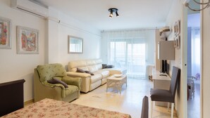 A well-lit room with a sofa, a chair, a small table, and a bed with a floral bedspread. - Apartment "Nav 4C 4pC" with Sea View & Terrace (Torrevieja)