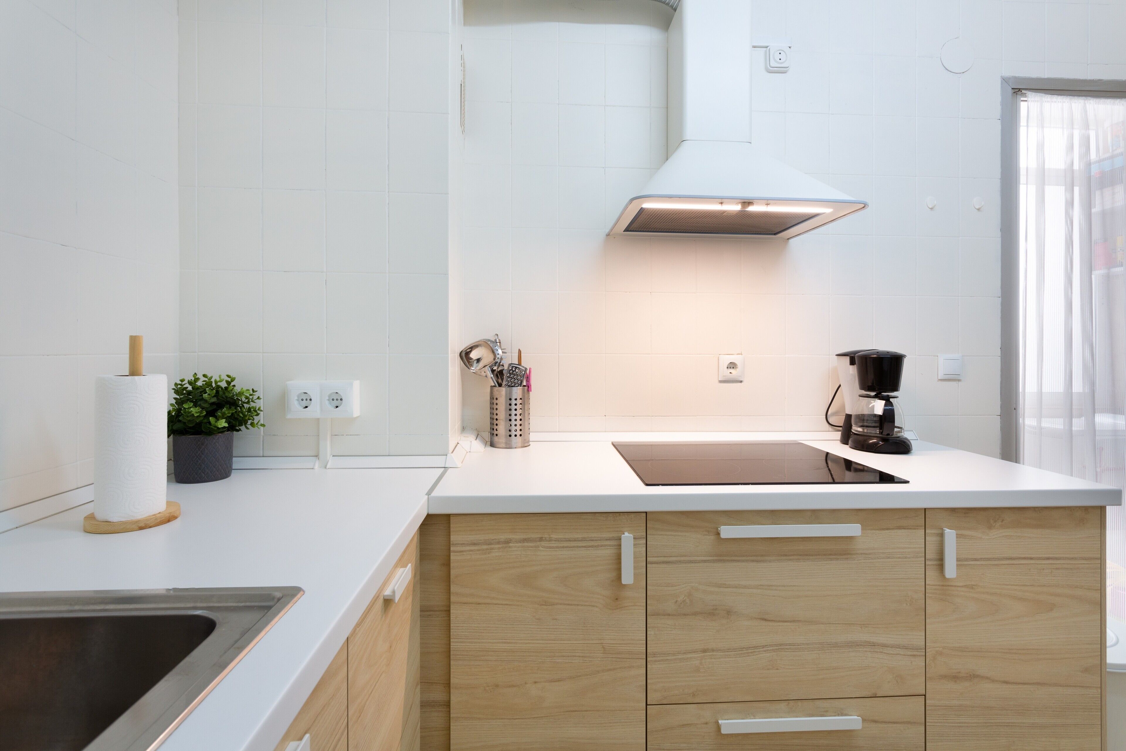 Una cocina moderna con encimera blanca, armarios de madera y pileta de acero inoxidable, además de una cafetera.