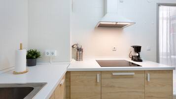 Una cocina moderna con encimera blanca, armarios de madera y pileta de acero inoxidable, además de una cafetera.