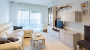 A living room with a sofa, a wicker coffee table, a television, and built-in shelving. - Apartment "Nav 4C 4pC" with Sea View & Terrace (Torrevieja)