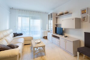 Una sala de estar con un sofá, una mesa de centro de mimbre, un televisor y estanterías empotradas.
