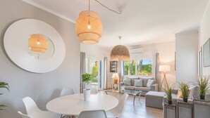Een moderne woonkamer met een ronde eettafel, witte stoelen, een bank en twee bijzettafeltjes met potplanten.