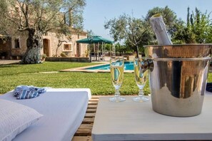 Un coin aménagé au bord de la piscine avec un lit, un seau de champagne et deux verres.