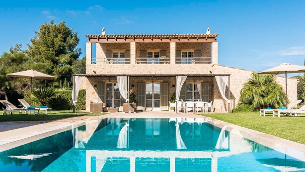 A stone building with a pool, outdoor seating, and a covered patio.
