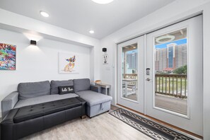 Relax in this stylish living room with a sofa, side table, and framed picture, leading to an outdoor deck with city views.