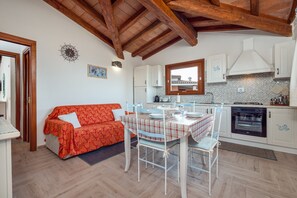 A compact kitchen with white cabinets, a dining table with chairs, a red sofa, and a wooden ceiling. - Apartment Zeus with Sea View, Balconies, Terrace and A/C (Tanaunella)