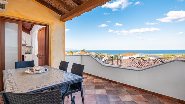 Un balcon avec une table et des chaises, une vue sur la mer et un bâtiment en arrière-plan.