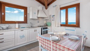 Une cuisine avec des meubles blancs, un plafond en bois et une table à manger dressée avec des assiettes et des verres.