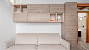 Una sala moderna con un sofá color beige, armarios de madera y una cocina visible a través de un umbral abierto.