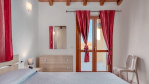 Un dormitorio con cama, mesita de noche, cómoda, silla, espejo y ventana con cortinas.