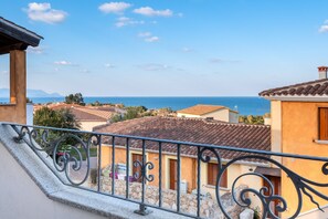 A balcony with a wrought iron railing overlooking a coastal town with terracotta-roofed buildings and a clear blue sky. - Holiday Apartment 'La Finestra sul Mare' with Sea View & Terrace (Budoni)