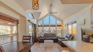 A spacious living room with a large window, a ceiling fan, and a dining area with a wooden table and chairs. - Gold Medal Trout Fishing at the Door - 2BR Cabin, 22mi to Breckenridge (Fairplay)