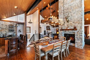 A spacious kitchen with a stone wall, wooden ceiling, and a fireplace.