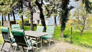 Ein Sitzbereich im Freien mit Tisch und Stühlen, umgeben von Bäumen und einem Zaun.