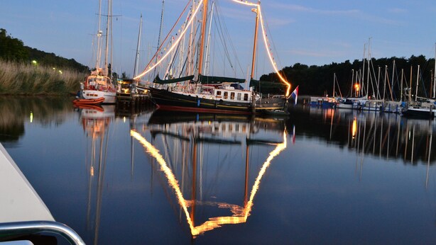 Ein ruhiger Hafen mit mehreren vertäuten Booten, einem klaren Himmel und ruhigem, schiffspiegelndem Wasser.