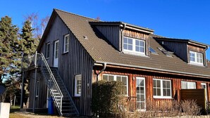 Ein zweistöckiges Holzhaus mit einer Metalltreppe, großen Fenstern und einer Garage.