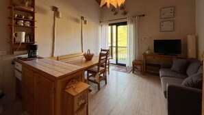 A cozy living room with a wooden dining table, chairs, a sofa, a television, and a balcony with curtains. - Duplex T2 apartment on slope for 6 people with ski box in Super-Sauze (Enchastrayes)