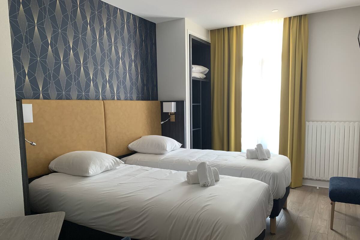 A hotel room with two beds, a wardrobe, a desk, and a window with curtains.