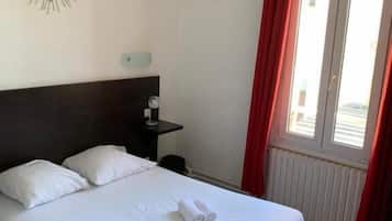 Une chambre d’hôtel avec un lit, des oreillers, une table de chevet, un élément de décoration murale, une fenêtre avec des rideaux rouges et une petite table.