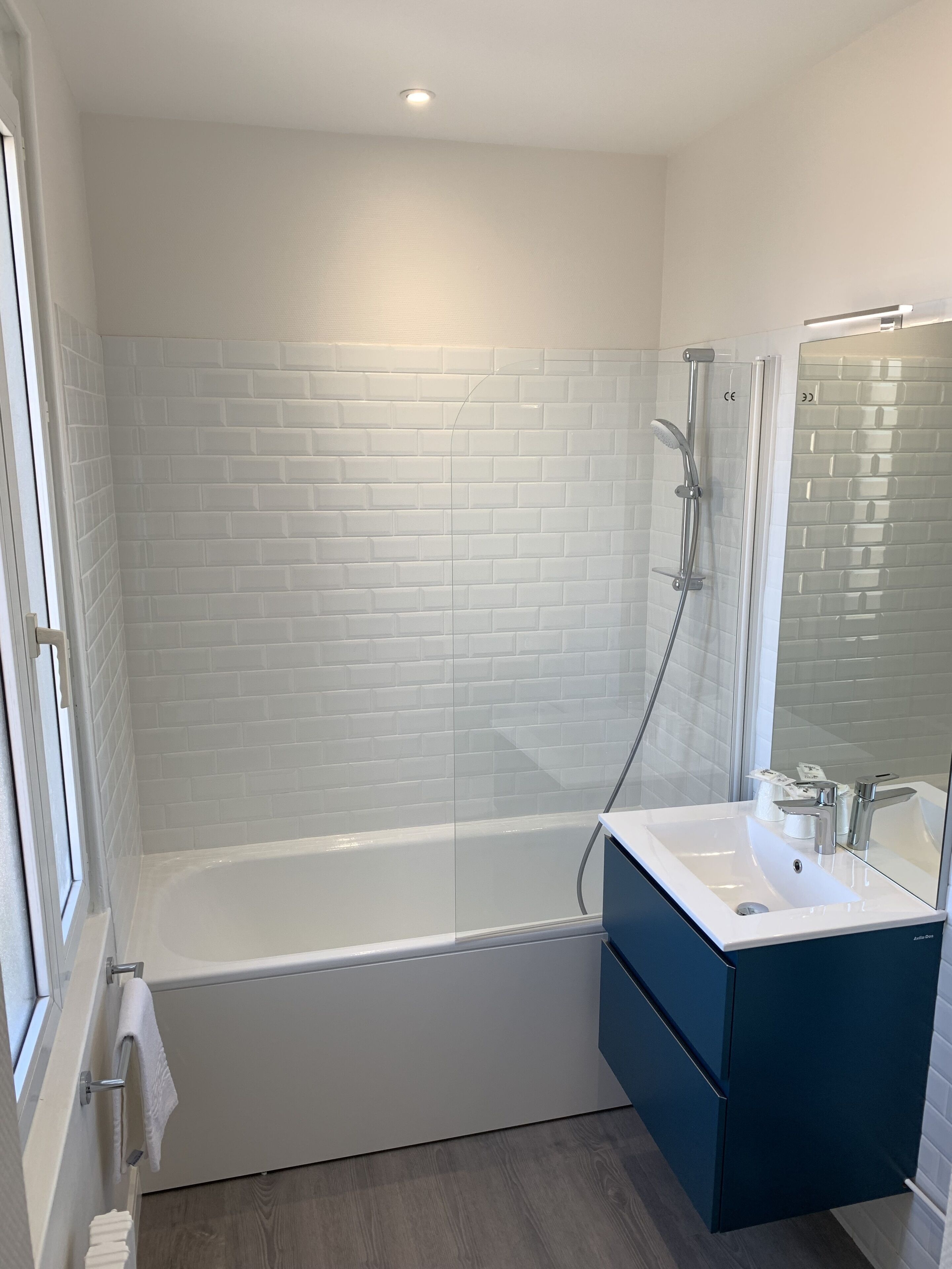 Ein modernes Badezimmer mit einer weißen Duschkabine, einer weißen Badewanne und einem dunkelblauen Waschtisch mit Spiegel.