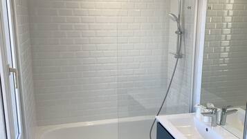 Ein modernes Badezimmer mit einer weißen Duschkabine, einer weißen Badewanne und einem dunkelblauen Waschtisch mit Spiegel.
