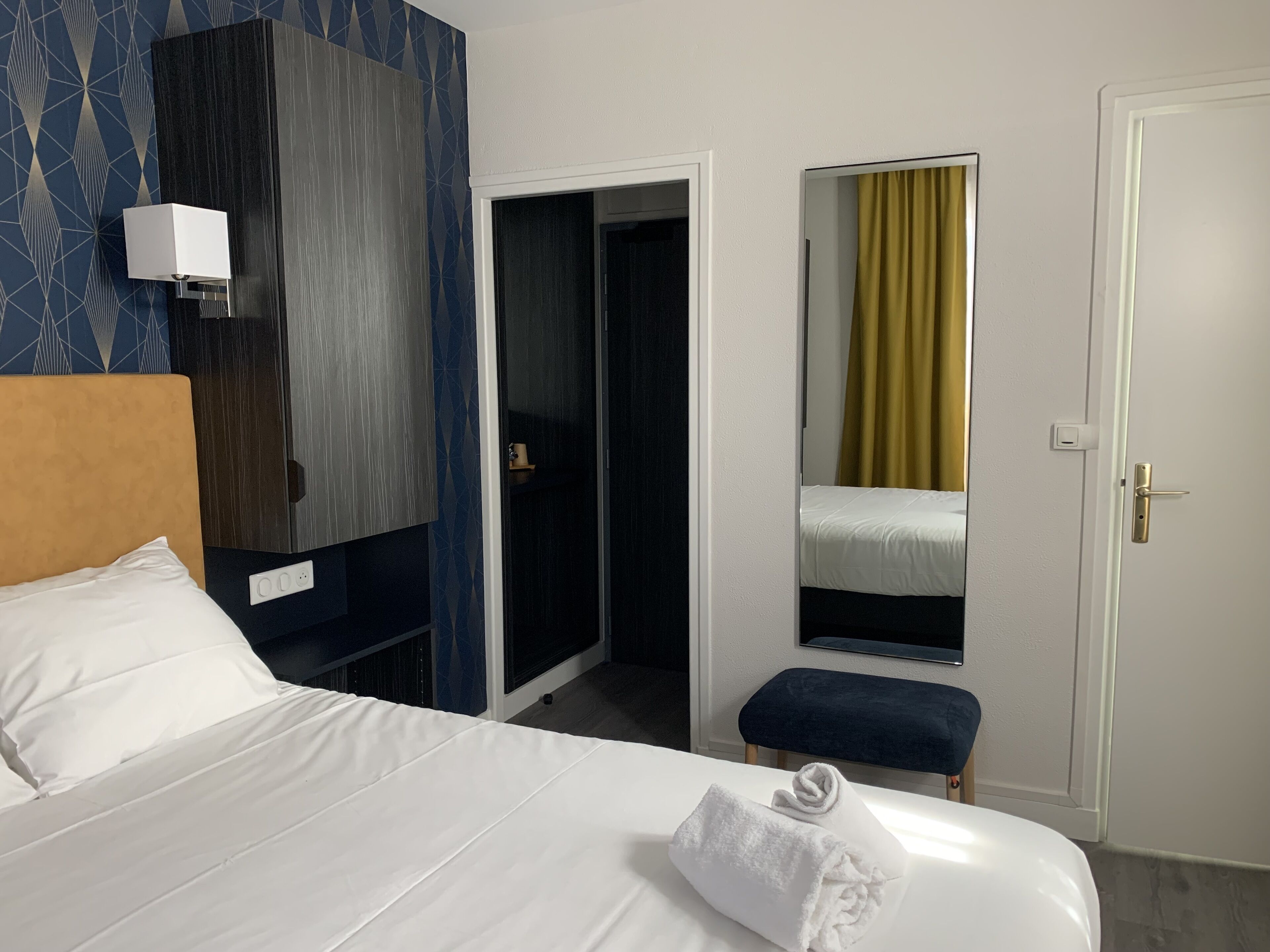A hotel room with a bed, a bedside table, a mirror, a wardrobe, and a door.